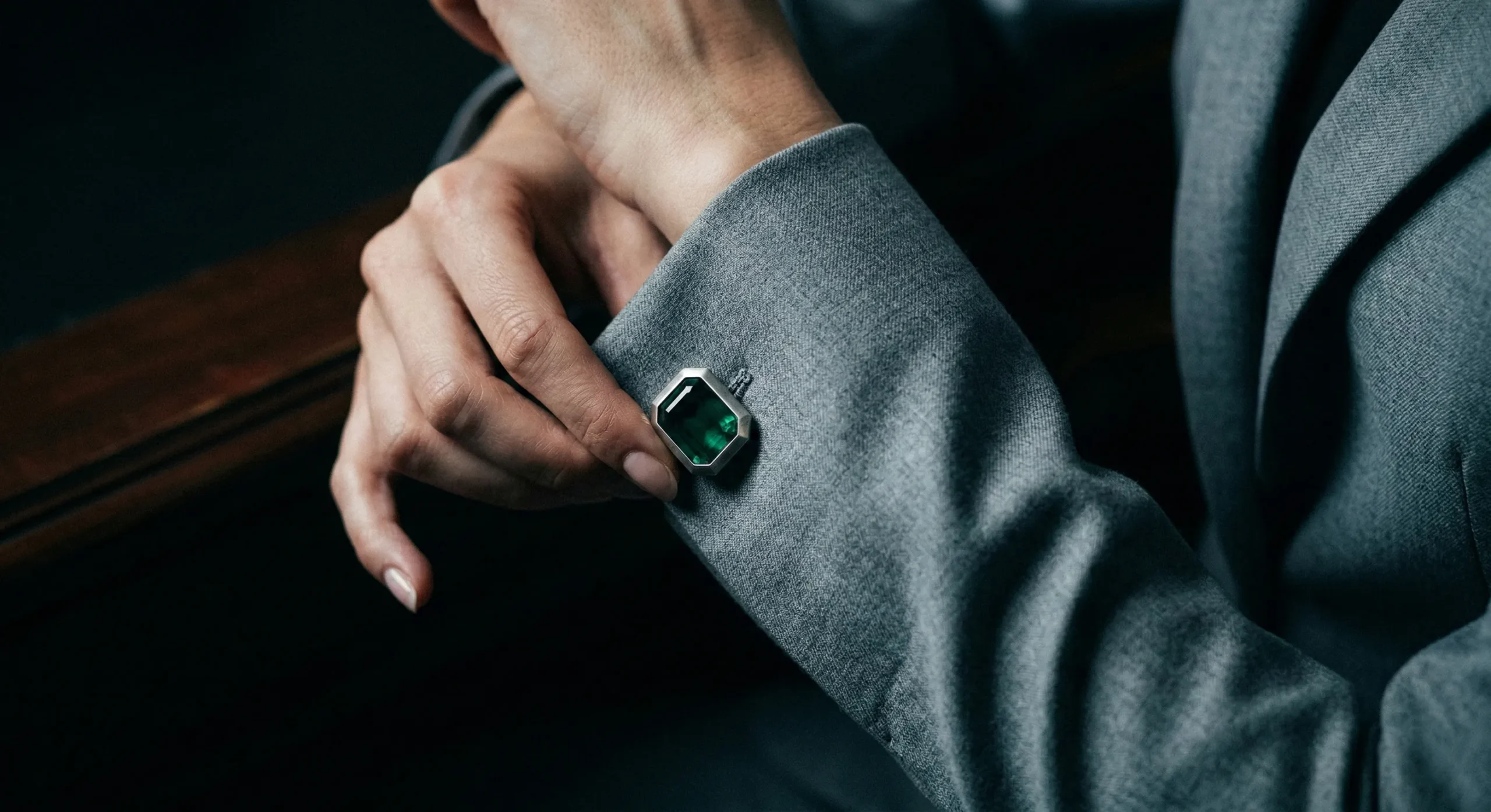 Woman's hand in dove-gray sleeve adjusting emerald cufflink in dramatic side lighting - ice queen CEO precision and control