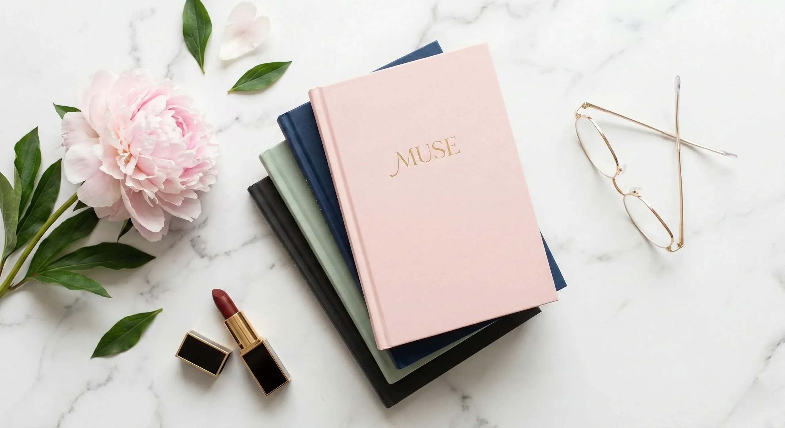 Stack of books with pastel and dark covers on white marble beside pink peony reading glasses and dark lipstick - sapphic romance rec list