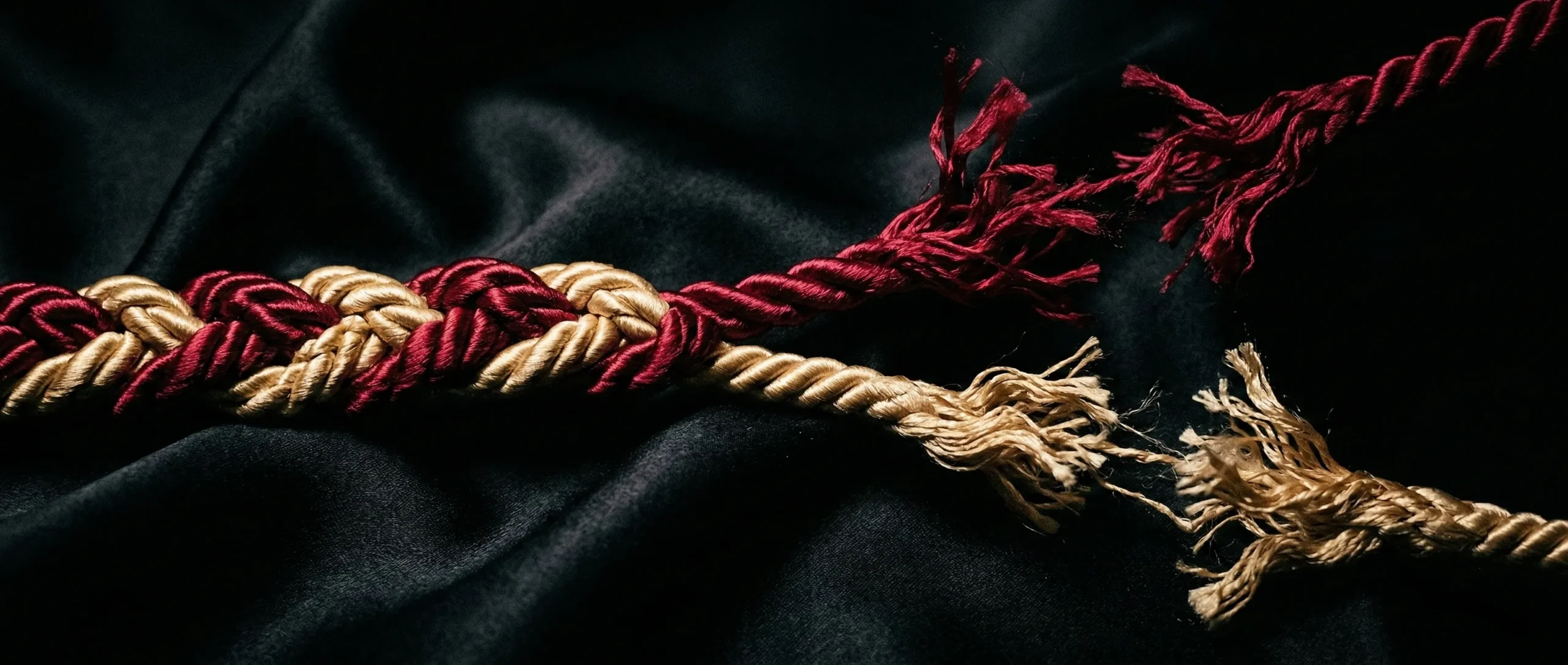Two silk ropes in crimson and gold intertwined then fraying apart on dark satin - sapphic BDSM connection and rupture