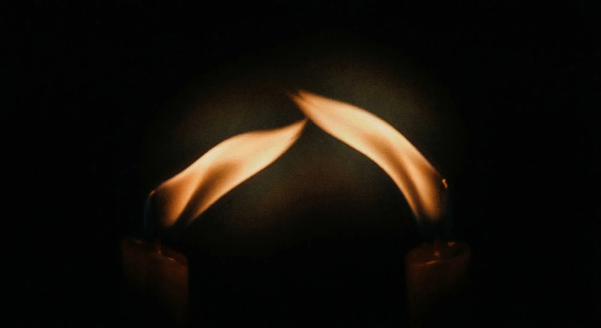 Two candle flames leaning toward each other in darkness — tension and attraction